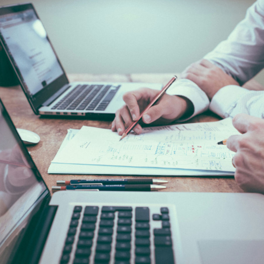 Business person taking notes in meeting with laptops and documents on desk