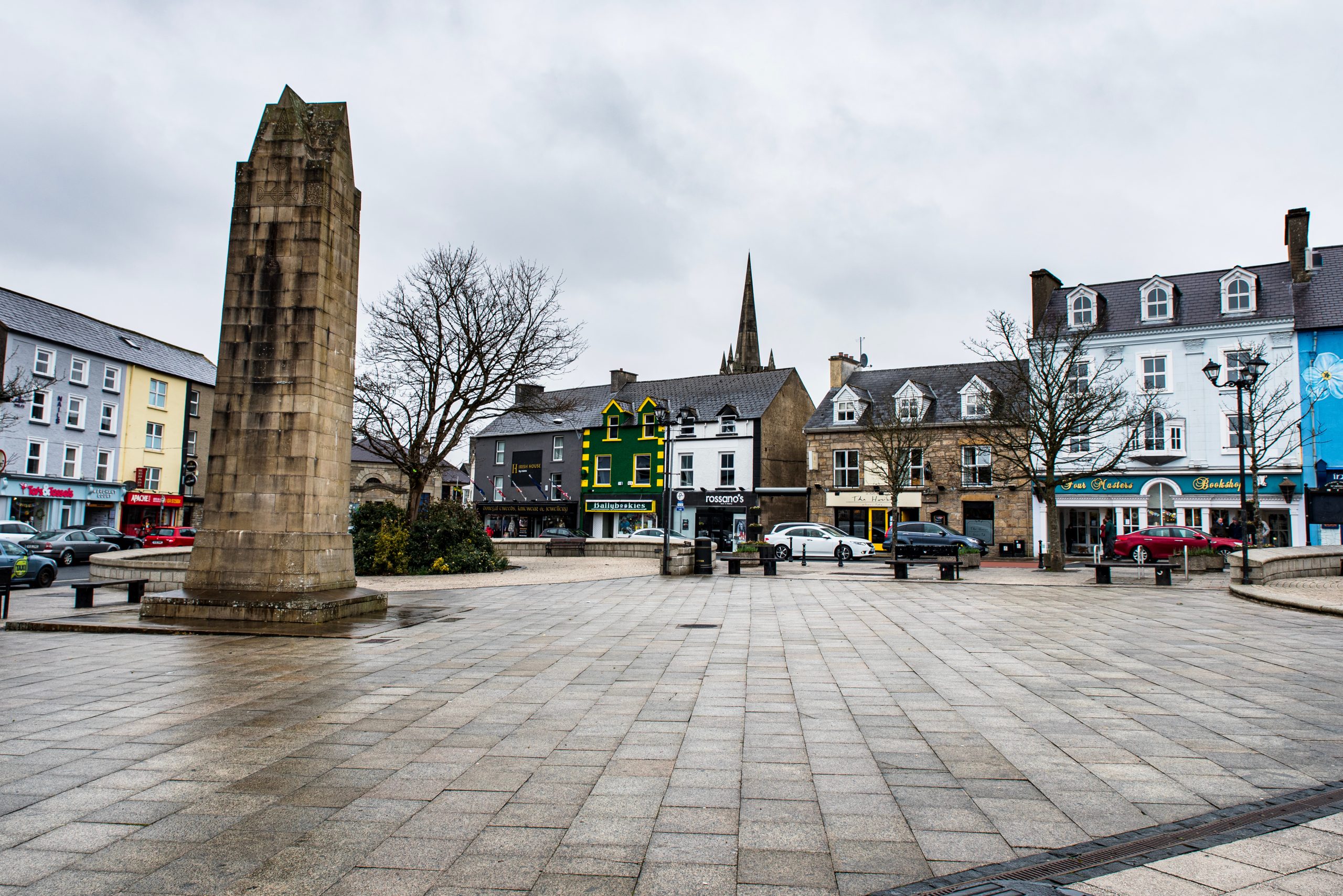 The Diamond, Donegal Town square in County Donegal, Ireland, with a stone obelisk, colorful shopfronts and a church spire on a rainy day.