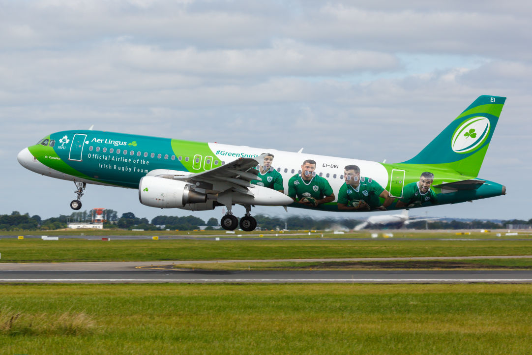 Aer Lingus Airbus A320 painted in green and white Irish Rugby Team livery with large player portraits and “#GreenSpirit” branding, lifting off from a runway under a cloudy sky